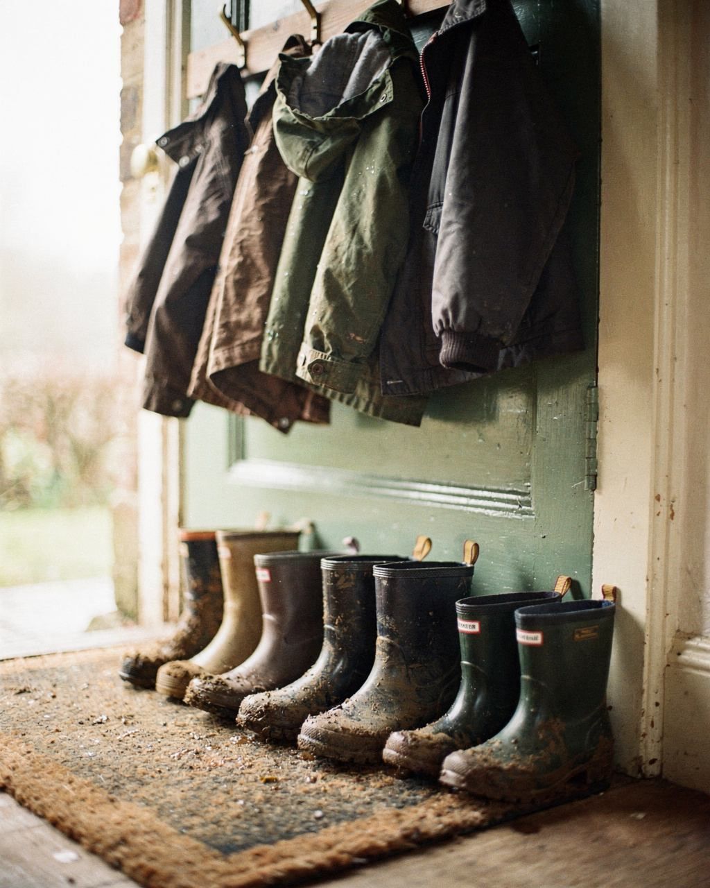 Muddy boots of different sizes lined up by a back door