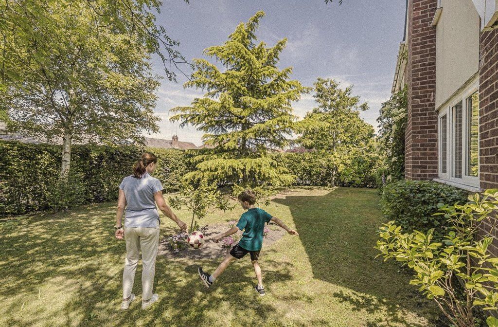 A carer and a boy playing football on a garden lawn