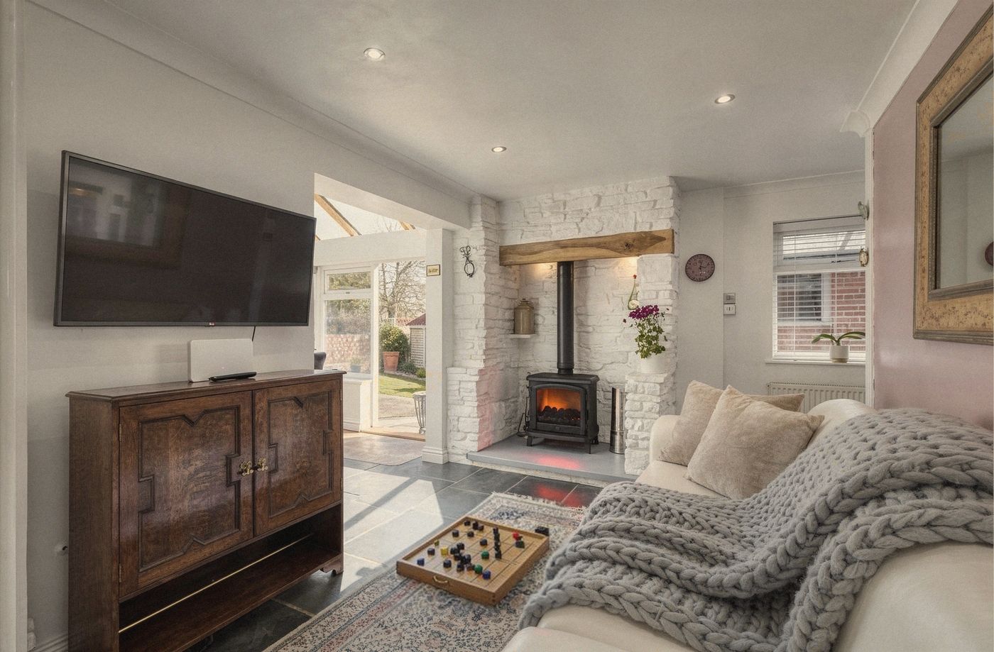 A sitting room with a wood burner glowing softly, a chunky knitted throw and a board game on the rug