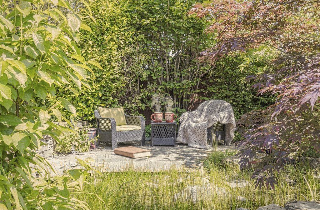 Garden chairs with a knitted blanket and a book, surrounded by greenery