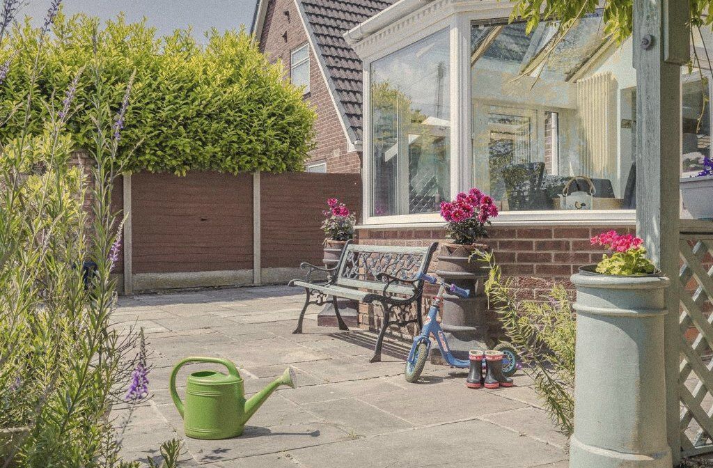 A sunny patio with a bench, a child's scooter and a watering can
