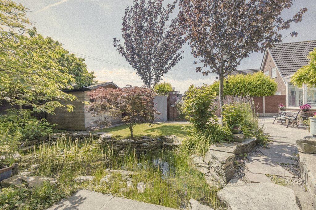 A back garden with a pond, rockery and flowering trees