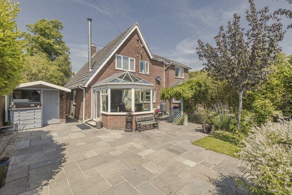 The back of a red-brick family house with a conservatory and a paved patio