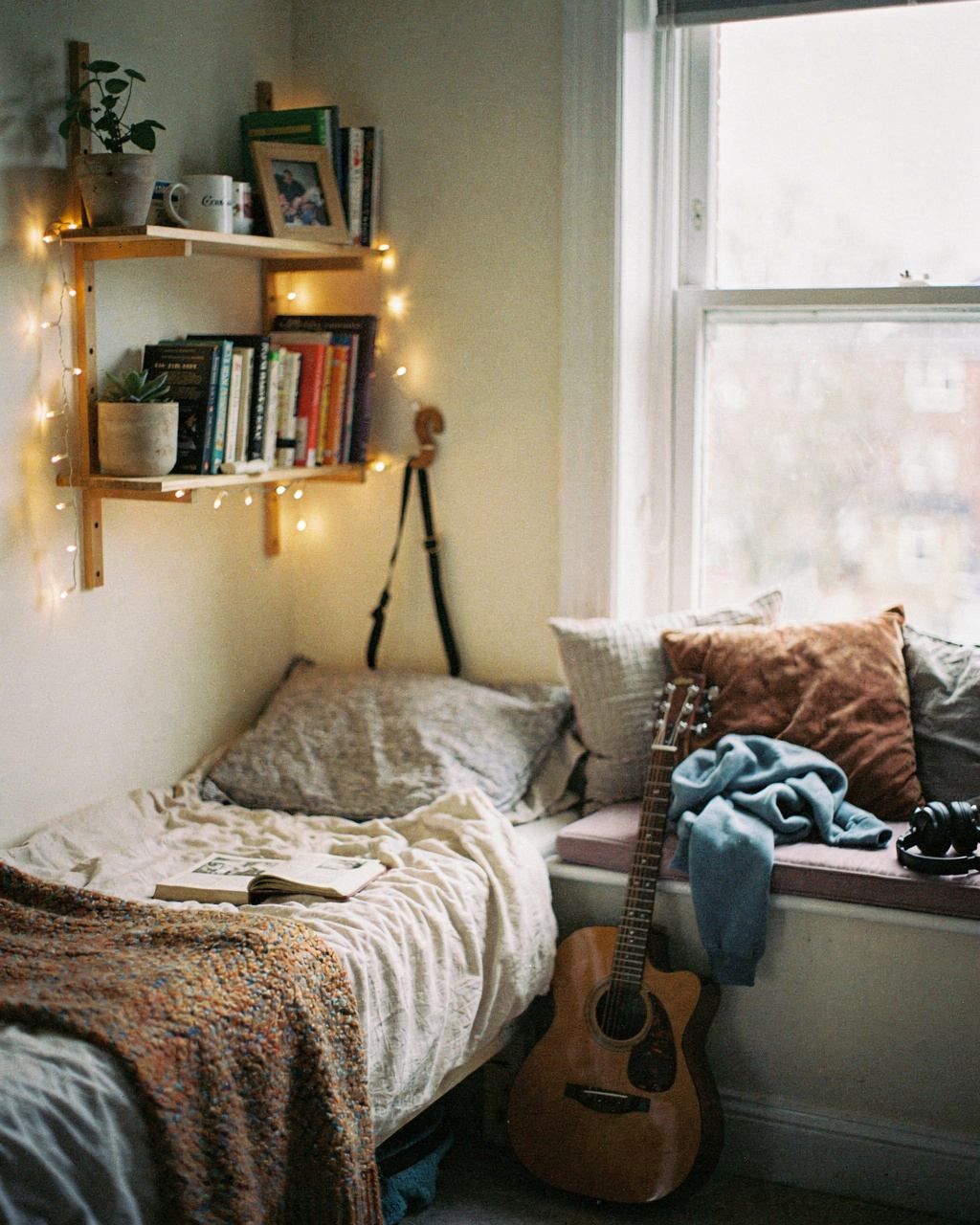 A young person's bedroom with a window seat, books and a guitar