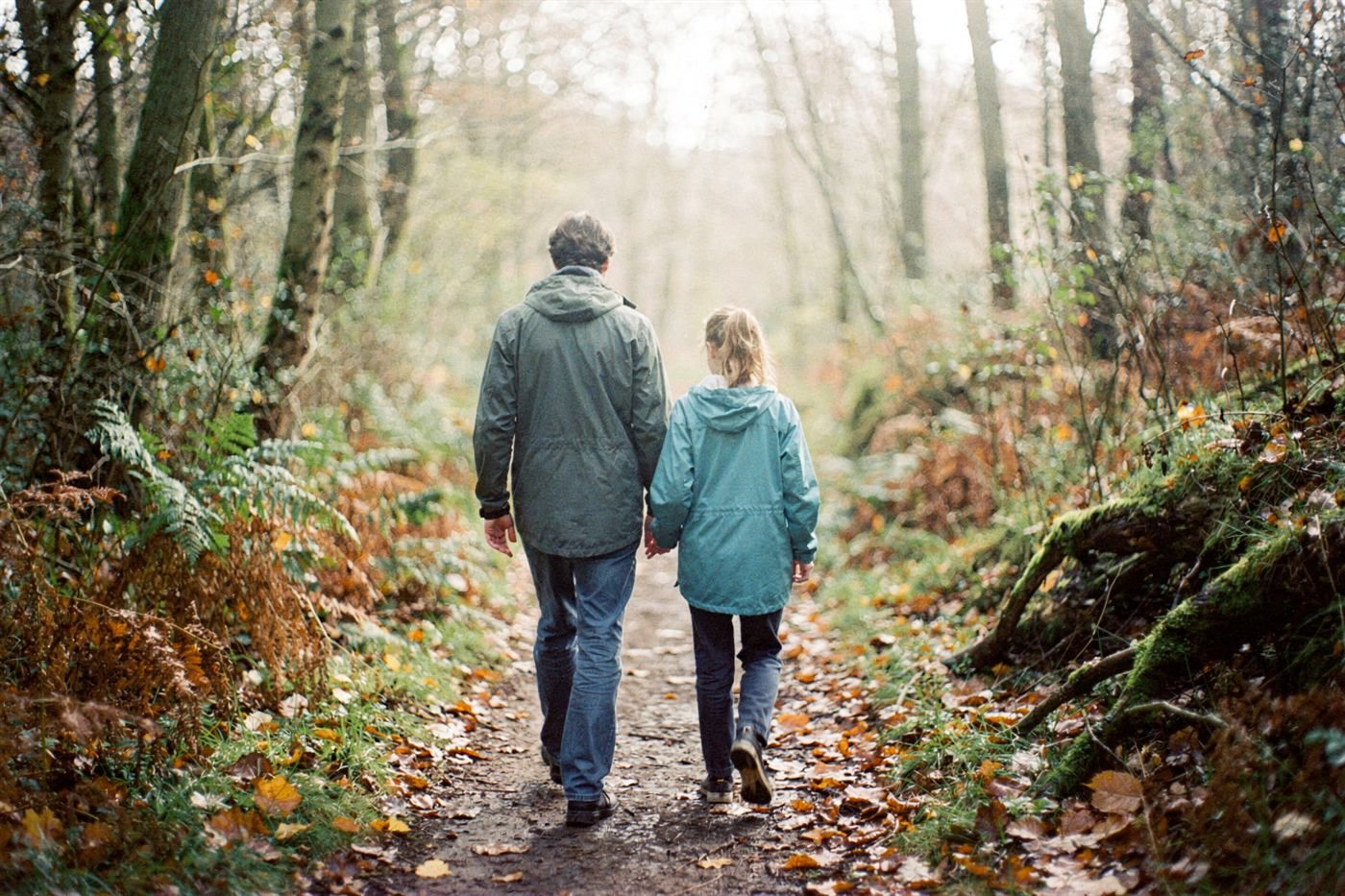 An adult and a young person walking together on a woodland path